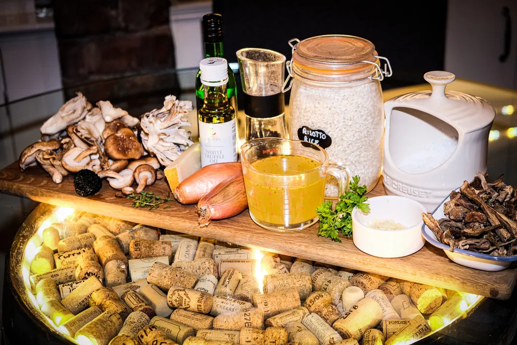 A wooden board with a small pile of dried porcini, fresh shiitake mushrooms, parmesan, parsley, a clove of garlic, and a slice of black truffle.