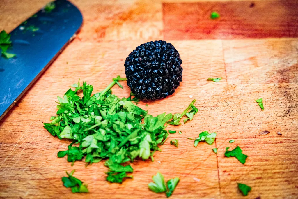 A small slice of black truffle alongside chopped parsley on a wooden board, ready to use.