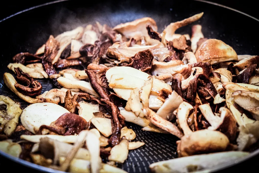 A frying pan with mushrooms browning, a wooden spoon and a knob of butter resting in the pan.