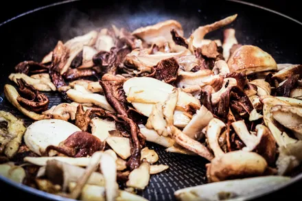 A frying pan with mushrooms browning, a wooden spoon and a knob of butter resting in the pan.