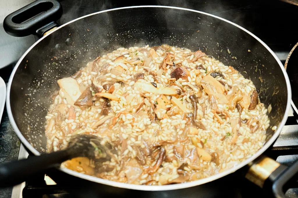A wide pan of arborio rice cooking in stock, the grains visibly absorbing the liquid.