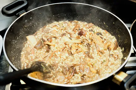 A wide pan of arborio rice cooking in stock, the grains visibly absorbing the liquid.