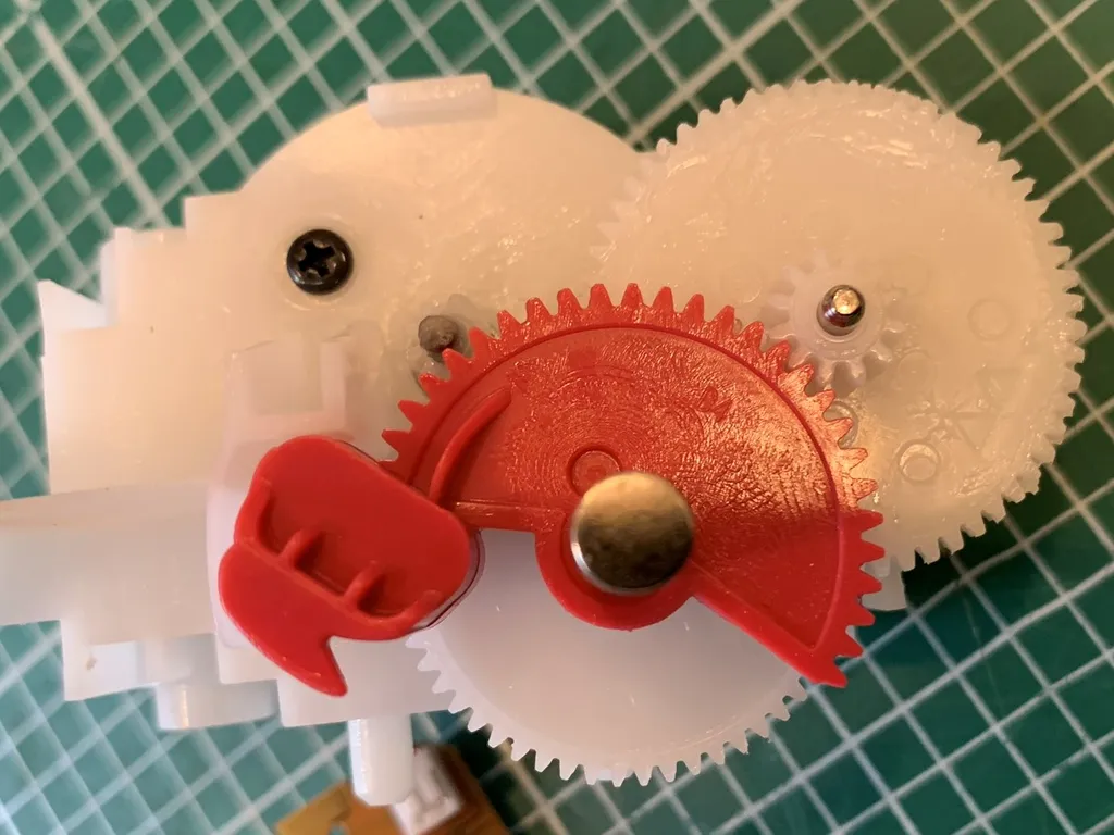 The internal gearing of an Airwick air freshener with the red plunger gear and the motor shaft visible.