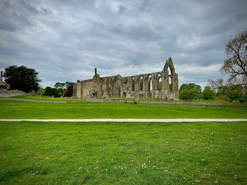 Bolton Abbey ruins stretching across a wide green lawn, the arched windows open to a soft overcast sky.