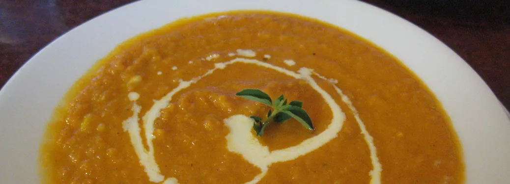 A wide white bowl of orange-gold carrot soup, finished with a swirl of double cream and a sprig of thyme.