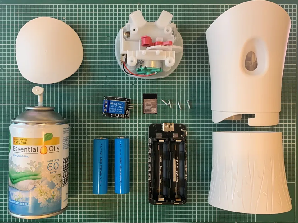 A flat-lay of the build components: an Airwick air freshener body, an ESP32 NodeMCU board, a 5V relay, a battery shield with two 18650 cells, and a small motor and gearing assembly.
