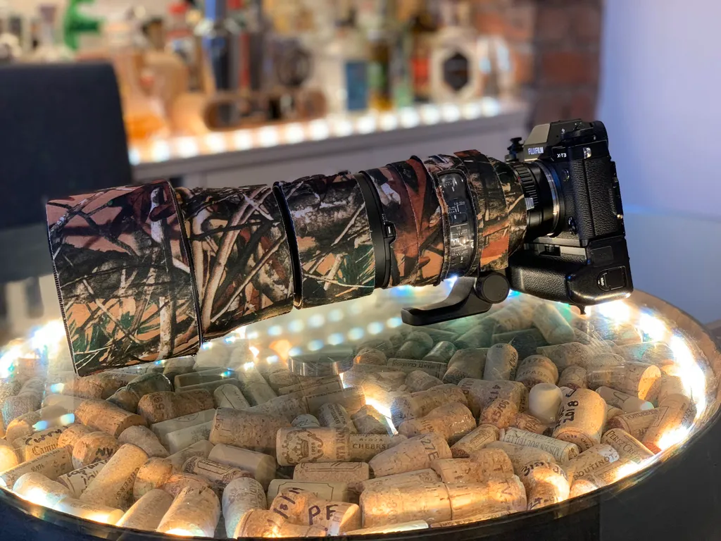 A Fujifilm X-T3 fitted with a camo-wrapped telephoto lens, resting on a bowl of wine corks.