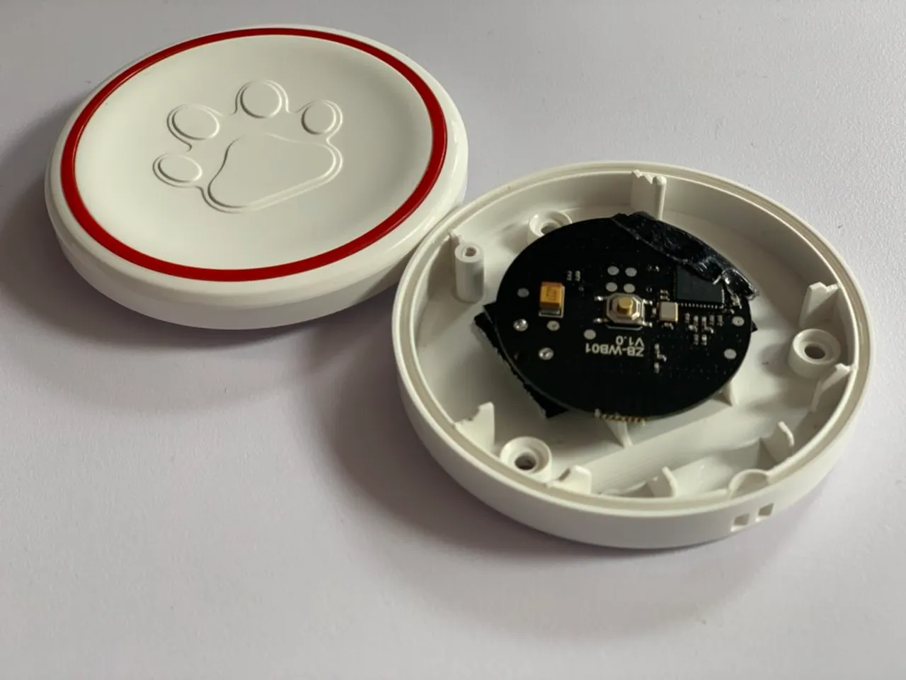 A finished paw-embossed dog training button on a wooden floor, the Sonoff Zigbee circuit hidden inside the original RF case.