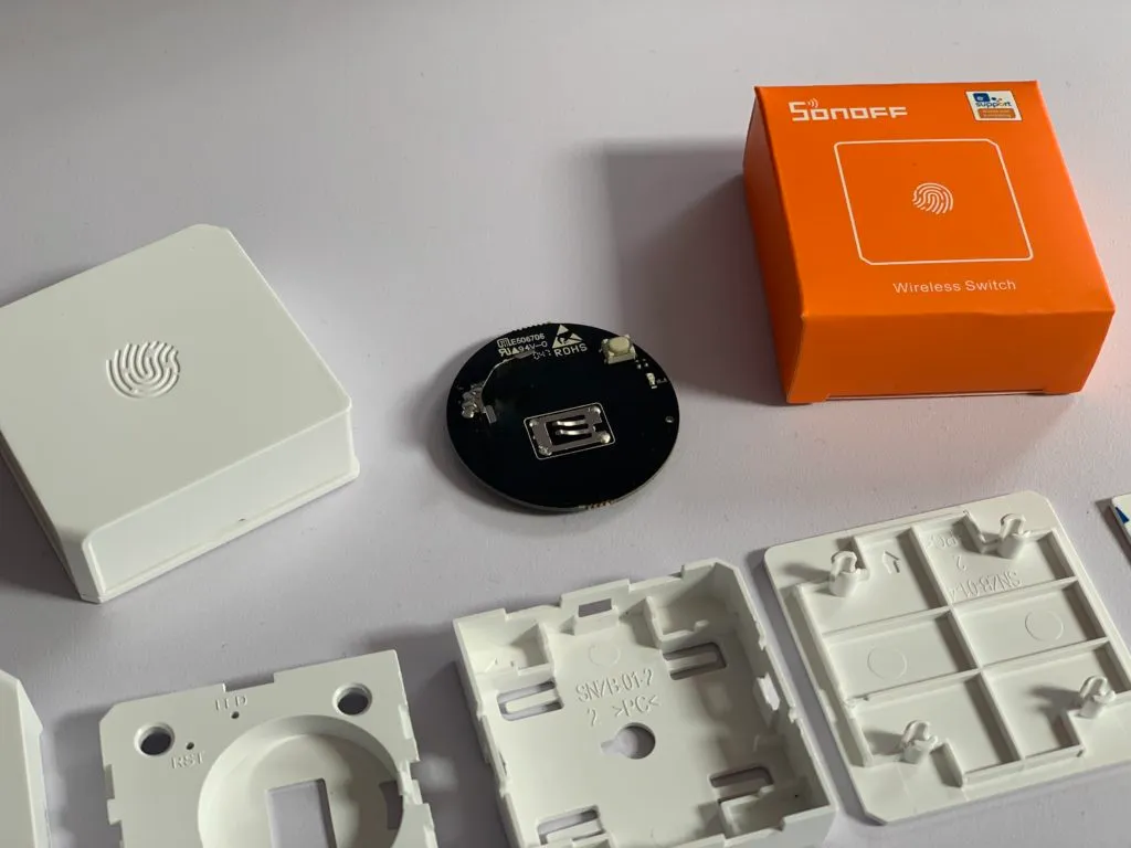 The Sonoff SNZB-01 Zigbee button circuit removed from its plastic case, with the coin-cell battery taped in place.